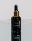 Black serum bottle with dropper labeled 'Bella Vida Santa Barbara Sunlight Serum with Acetyl Hexapeptide-8 and Bakuchiol on a reflective surface.