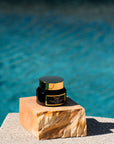 A jar of Brighten vitamin c cream by Bella Vida Santa Barbara jar with a black and gold label on a marble-like surface, placed near a pool.