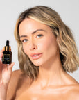 Woman holding a Black serum bottle with dropper labeled 'Bella Vida Santa Barbara Sunlight Serum with Acetyl Hexapeptide-8 and Bakuchiol
