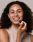 Woman holding a black lipstick against a neutral background