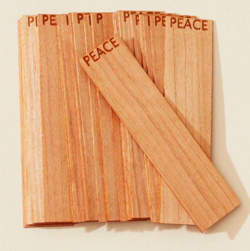 Wooden candle wicks with 'PEACE' engraved on them against a beige background
