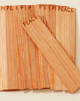 Wooden candle wicks with 'PEACE' engraved on them against a beige background